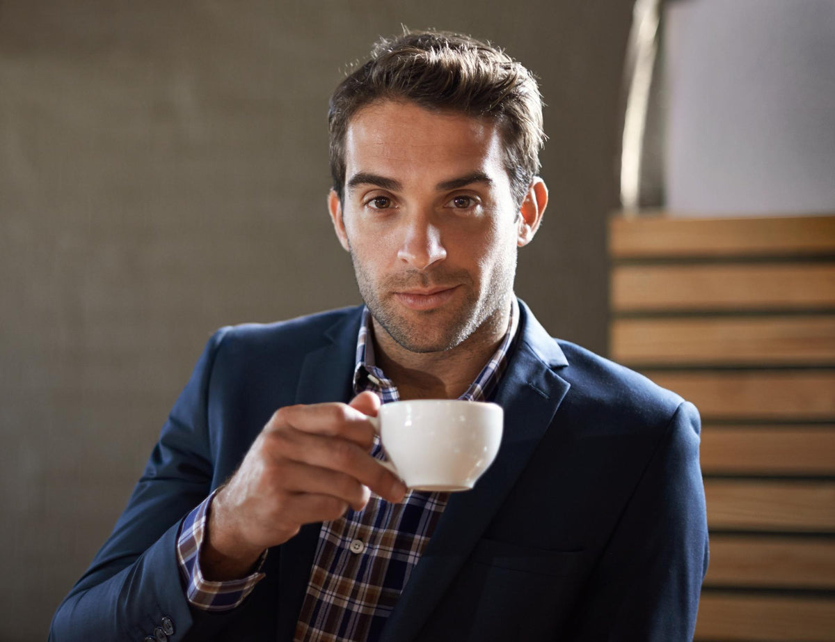 A man in a navy blue blazer and plaid shirt holding a white ceramic coffee cup, representing Noah Bennett's customer review for PsyKey functional coffee.